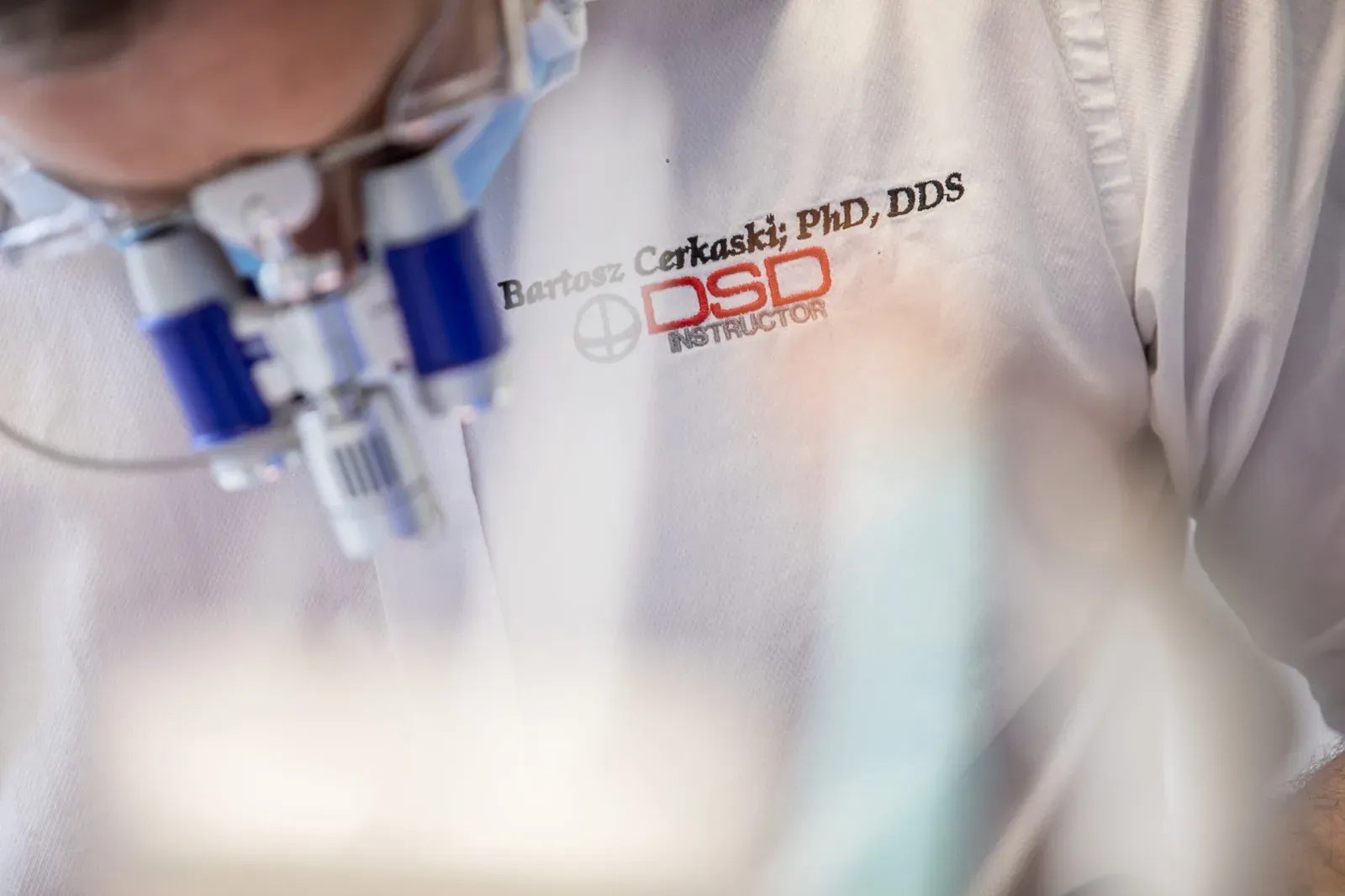 Bartosz Cerkaski podczas pracy klinicznej w lupach zabiegowych — kitel z haftem Bartosz Cerkaski PhD, DDS — DSD Instructor